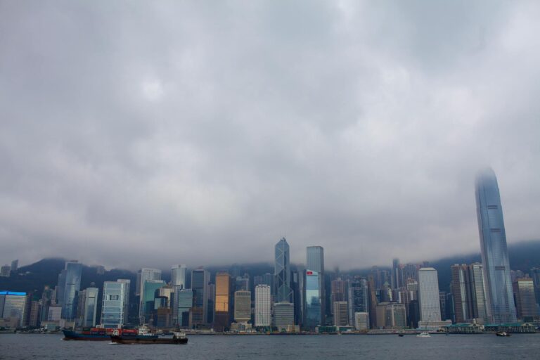 Dramatic urban skyline of Hong Kong under a cloudy sky, showcasing Victoria Harbour.