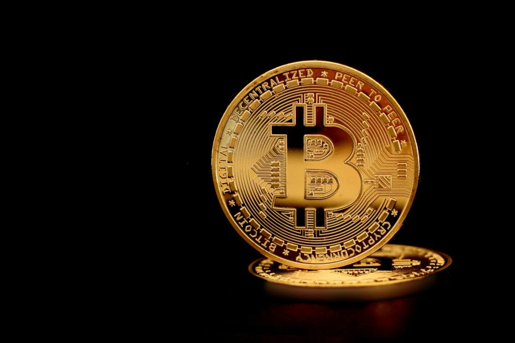 Close-up of a golden Bitcoin coin reflecting light on a dark backdrop, symbolizing digital currency and wealth.