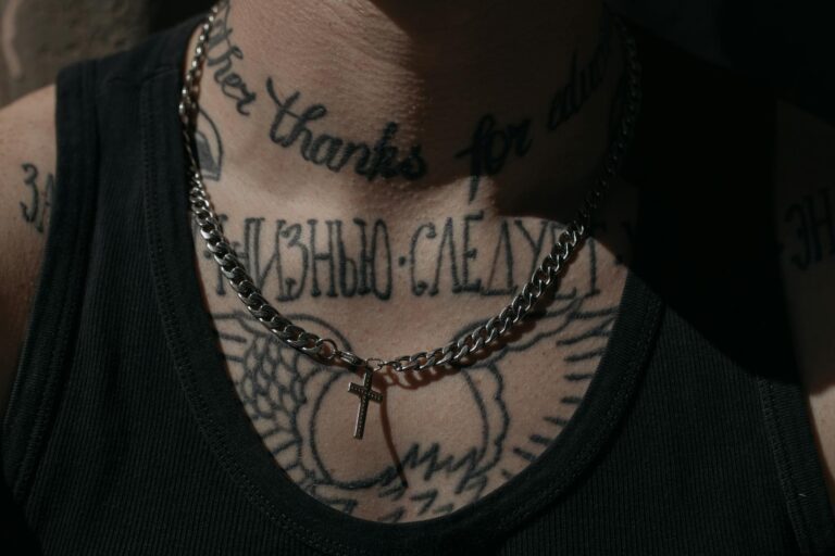 Detailed view of tattoos and cross pendant on a person's chest wearing a tank top.